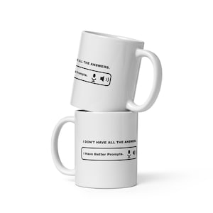 May include: Two stacked white ceramic mugs featuring black text that reads I DON'T HAVE ALL THE ANSWERS and I Have Better Prompts, accompanied by a black microphone icon and a speaker icon inside a rectangular border on each mug.