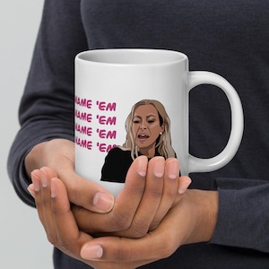 Puede incluir: Taza de cerámica blanca con una ilustración rosa y negra de una mujer con cabello rubio que dice "Name 'em" repetidamente.