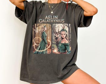 May include: A dark gray oversized t-shirt with a graphic print of a woman in a green dress and a deer in a forest. The text "Aelin Galathynius" and "To Whatever End" is printed on the shirt.