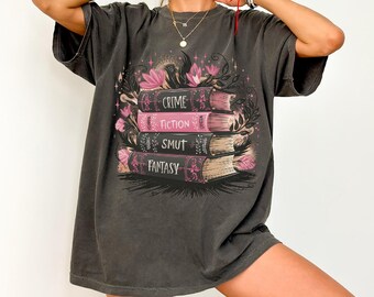 May include: A dark gray oversized t-shirt with a graphic print of a stack of books with the words "Crime", "Fiction", "Smut", and "Fantasy" on the spines. The books are surrounded by pink flowers and leaves.