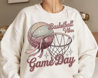 May include: White sweatshirt with a pink basketball and hoop graphic. The text "Basketball Vibes Game Day" is printed in pink.