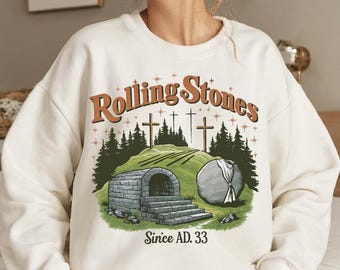May include: White sweatshirt with a graphic print of a stone tomb with a rolling stone in front of it. The text "Rolling Stones Since AD. 33" is printed below the image.