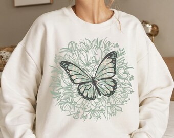 May include: White sweatshirt with a green and black butterfly graphic. The butterfly is surrounded by a circle of green flowers.