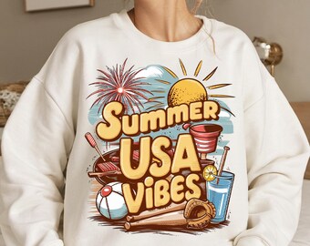 May include: Cream-colored sweatshirt with a colorful graphic design. The design features the text "Summer USA Vibes" with illustrations of a sun, fireworks, a grill, a baseball, a drink, and a baseball glove. The sweatshirt is a casual summer style.