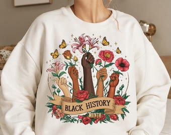 May include: White sweatshirt with a graphic design of raised fists holding flowers and a banner that reads "Black History Month".