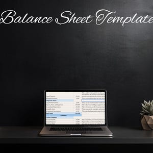 Pode incluir: Um computador portátil com um modelo de balanço aberto na tela. O laptop está em uma mesa preta com uma pilha de cadernos e uma planta suculenta em vaso.