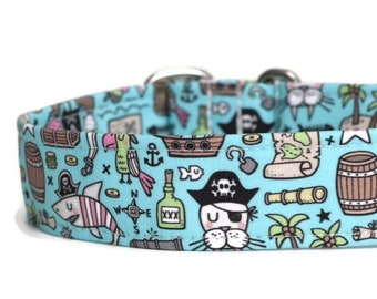 May include: A light blue dog collar with a pirate-themed pattern. The pattern includes a parrot, a ship, a treasure chest, a compass, a skull and crossbones, a shark, a bottle of rum, a palm tree, and a pirate cat. The collar is made of durable fabric and has a silver buckle.