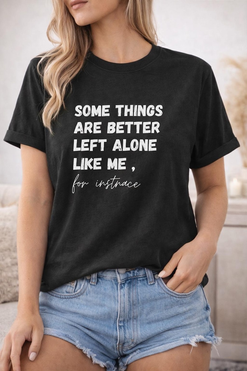 May include: Black t-shirt with white text that reads "SOME THINGS ARE BETTER LEFT ALONE LIKE ME, for instance." The shirt is paired with denim shorts. The model is wearing the shirt and shorts.