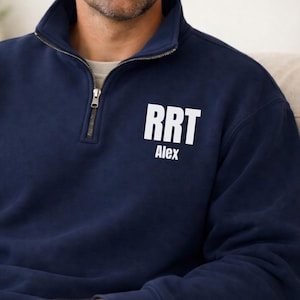 Puede incluir: Sudadera azul marino con cremallera de un cuarto de cuello, con las letras "RRT" y el nombre "Alex" impresos en blanco. La sudadera tiene cuello y puños acanalados. La cremallera es plateada.