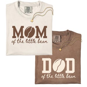 May include: Two crew neck t-shirts, one off-white with brown text reading MOM of the little bean and one brown with off-white text reading DAD of the little bean, both featuring a coffee bean graphic replacing the letter O in each word.