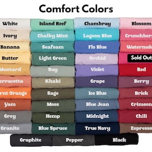 May include: A color chart titled Comfort Colors displaying a grid of folded t-shirts in various shades including white, ivory, banana, butter, mustard, terracotta, burnt orange, yam, grey, granite, island reef, chalky mint, seafoam, light green, bay, khaki, sage, moss, hemp, blue spruce, chambray, lagoon blue, flo blue, orchid, violet, grape, ice blue, blue jean, midnight, true navy, blossom, crunchberry, watermelon, red, berry, brick, crimson, chili, espresso, graphite, pepper, and black, with one label marked Sold Out.