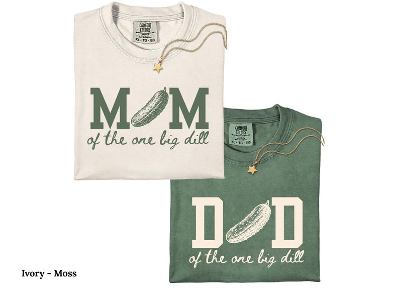 May include: An ivory t-shirt with dark green text reading MOM of the one big dill and a moss green t-shirt with ivory text reading DAD of the one big dill. Both shirts feature a pickle graphic replacing the letter O and a gold star necklace.