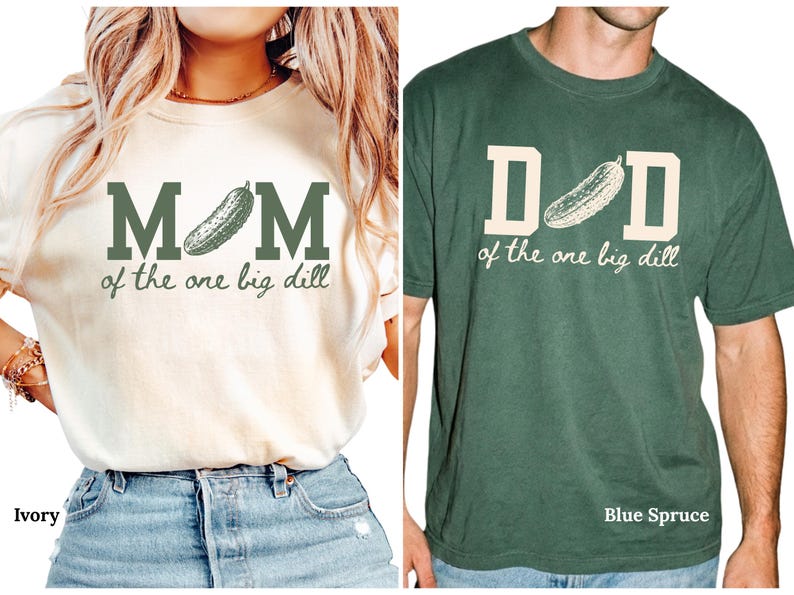 May include: An ivory t-shirt with dark green text reading MOM of the one big dill featuring a pickle graphic, and a blue spruce t-shirt with cream text reading DAD of the one big dill featuring a pickle graphic, both with short sleeves.