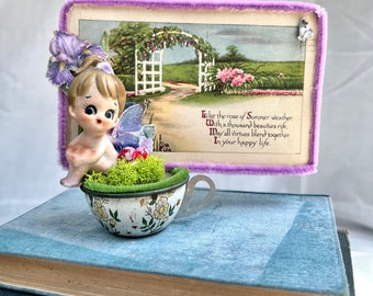 Vintage Spring postcard with a porcelain fairy in a tin tea cup.