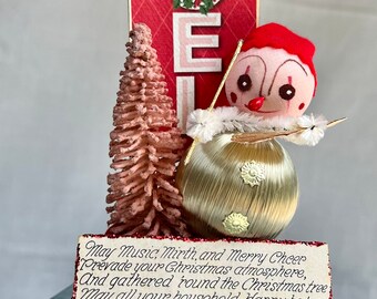 Vintage Christmas elf atop a jello tin with a "Noel" card