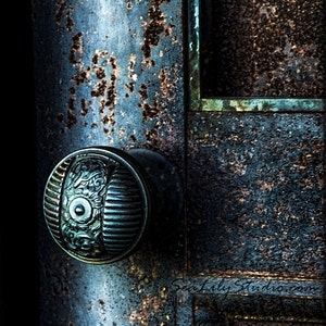 May include: A close-up of a vintage door knob with intricate details. The knob is made of metal and has a dark blue finish. The door is made of wood and has a rustic, weathered look. The door is covered in rust and has a worn, aged appearance.