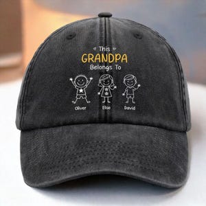 May include: A black baseball cap with the text "This Grandpa Belongs To" in yellow, with three stick figure children's drawings below. The children's names, Oliver, Elise, and David, are printed below each figure.