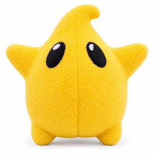 May include: A bright yellow plush toy shaped like a star with a pointed top. The soft fabric has a textured surface. It features two large, oval-shaped black eyes with small white highlights positioned near the center of the star-shaped body.