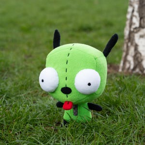 K&ouml;nnte beinhalten: Ein gr&uuml;ner Pl&uuml;schcharakter mit gro&szlig;en wei&szlig;en Augen, schwarzen Antennen und einer roten Zunge. Die Puppe hat ein gen&auml;htes Design und schwarze Arme und Beine. Es befindet sich vor dem Hintergrund von gr&uuml;nem Gras und einem Baum.