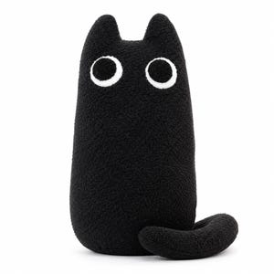 May include: A plush toy shaped like a cat, crafted from black textured fabric. The cat features two pointed ears at the top and two large, circular eyes with white outlines and black centres. A curved black tail extends from the lower right side.