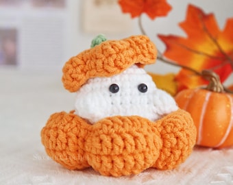 May include: A handmade crochet pumpkin ghost with a white body, orange pumpkin shell, and a green stem. The ghost has black button eyes and is sitting on a white surface. A small orange pumpkin is in the background.