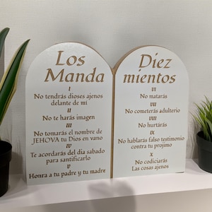 May include: Two white wooden plaques with rounded tops, each with a brown wooden frame. The left plaque has the text "Los Mandamientos" and lists the first five commandments in Spanish. The right plaque has the text "Diez Mientos" and lists the last five commandments in Spanish.