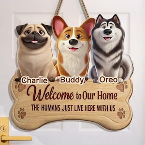 Puede incluir: Letrero de madera con forma de hueso de perro con tres perros de dibujos animados: un pug, un corgi y un husky. El letrero dice "Bienvenido a nuestro hogar" con los nombres "Charlie", "Buddy" y "Oreo".