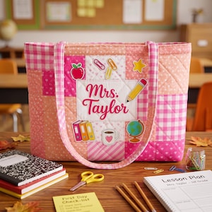 May include: A quilted tote bag in shades of pink and peach with a patchwork design. The center features a white panel with the text Mrs. Taylor, surrounded by colorful school-themed graphics including an apple, paperclips, star, pencil, books, mug, and globe.