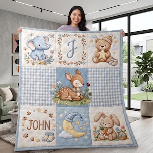 May include: A quilted baby blanket featuring a grid of nine panels with illustrations of a blue elephant, a teddy bear with a star, a deer, a crescent moon, and a rabbit. The quilt includes the letter J and the name JOHN in brown text.