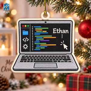 May include: A laptop-shaped Christmas ornament featuring a black screen with colorful lines of code, a white cursor, and the name Ethan embroidered in white. The keyboard area is silver with a black trackpad, all outlined in a cream-colored border.