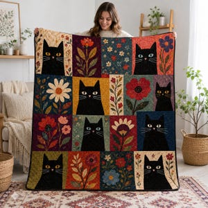 May include: A rectangular quilt featuring a grid pattern of alternating panels. The panels display illustrations of black cats with yellow eyes and various colorful floral arrangements including daisies, poppies, and wildflowers on textured backgrounds.