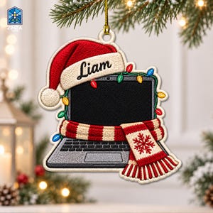 Peut inclure: Une décoration de Noël brodée et plate en forme d'ordinateur portable. L'ordinateur est orné d'un bonnet de Père Noël rouge et blanc portant le nom Liam, d'une écharpe rayée rouge et blanche avec un flocon de neige et de guirlandes lumineuses.