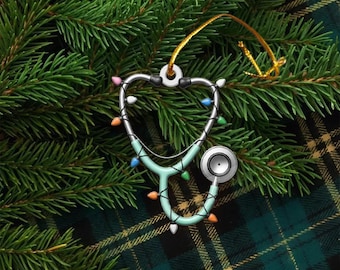May include: A stethoscope-shaped Christmas ornament with a silver frame and a light blue tube. The ornament is decorated with colorful Christmas lights and a gold string for hanging. The ornament is displayed on a bed of green pine needles.