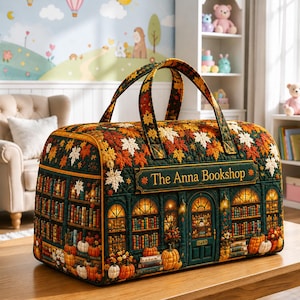 Op de afbeelding: Een gewatteerde reistas met een print van een donkergroene boekwinkelgevel met boekenplanken, pompoenen en herfstbladeren. De tekst The Anna Bookshop staat op een rechthoekig bord aan de voorzijde. De tas heeft twee handvatten en een ritssluiting.