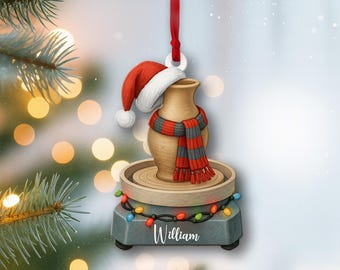 Può includere: Un ornamento natalizio in ceramica raffigurante un tornio da vasaio con un vaso con cappello e sciarpa di Babbo Natale. La base grigia porta il nome "William" e luci colorate. Un nastro rosso è attaccato.