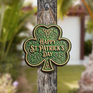 Op de afbeelding: Een groen klavervormig bord met de tekst "Happy St. Patrick's Day" in gouden letters. Het bord heeft een gouden touwachtige rand en Keltische knoop- en klaverdetails. Het hangt aan een houten paal.