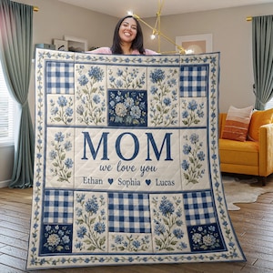 May include: A quilted blanket with a floral and gingham pattern in shades of blue and cream. The word "MOM" is displayed prominently, with "we love you" and names below. A decorative and personalized gift.