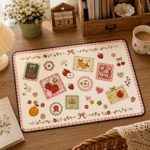 May include: A rectangular desk mat with a cream-colored background featuring a repeating pattern of strawberries, cherries, oranges, flowers, and hearts in various square and circular frames, bordered by a pink and white checkered edge.