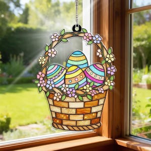 May include: A stained glass Easter basket with three colorful eggs and floral accents. The basket is brown with a textured design, and the eggs are decorated with stripes and patterns. The window hanging is suspended by a chain.