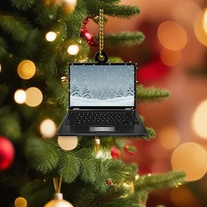 May include: A black laptop Christmas tree decoration, with a winter landscape on the screen, suspended by a gold cord. The laptop screen shows a snowy forest scene. The name "Sophia" is printed on the laptop.