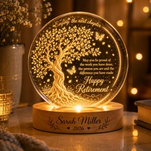 May include: A circular glass plaque with an illuminated tree design, butterflies, and the text: Enjoy the next chapter. May you be proud of the work you have done, the person you are and the difference you have made. Happy Retirement. The wooden base reads Sarah Miller 2026.