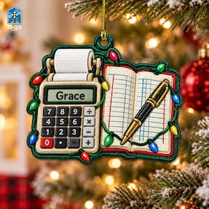Op de afbeelding: Een hangend ornament in de vorm van een rekenmachine met een papierrol en een open kasboek met een pen. Het scherm van de rekenmachine toont de naam Grace. Het ontwerp is versierd met een snoer van kleurrijke kerstverlichting.