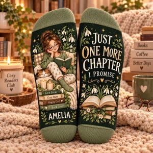 May include: A pair of dark green socks featuring a graphic of a person reading a book with a cat, the name Amelia, and the text Just One More Chapter I Promise, surrounded by illustrations of snowdrop flowers and stacked books.