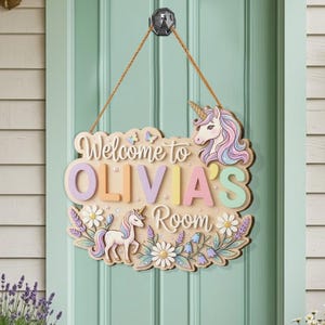May include: Wooden sign saying "Welcome to OLIVIA'S Room". The sign features a unicorn, flowers, and butterflies in pastel colours. It hangs from a brown rope and is mounted on a light green door.