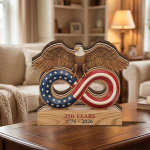 May include: A wooden sculpture featuring an American bald eagle perched atop an infinity symbol with the American flag design. The base reads "250 YEARS 1776-2026". The sculpture is made of layered wood with intricate details and patriotic colors.