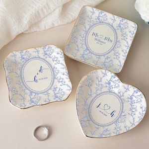 May include: Three ring dishes in square, heart, and scalloped shapes. Each dish features a blue and white floral pattern, with gold trim. The dishes have personalized text in the centre, including initials and dates.