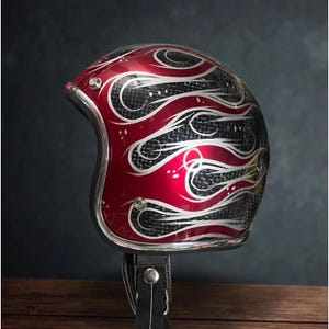 Może przedstawiać: Czerwony kask motocyklowy ze srebrnym wykończeniem i czarnym paskiem pod brodą. Kask ma wzór płomieni w kolorze srebrnym i białym na wzorze z włókna węglowego. Zaprojektowany z myślą o bezpieczeństwie i stylu.