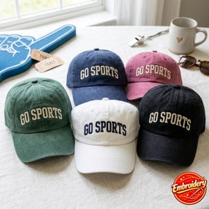 Può includere: Cinque cappellini da baseball in verde, blu navy, bianco, rosa e nero. Ogni cappellino presenta la scritta GO SPORTS ricamata in un colore a contrasto sul pannello frontale. I cappellini hanno una corona strutturata e una visiera curva.