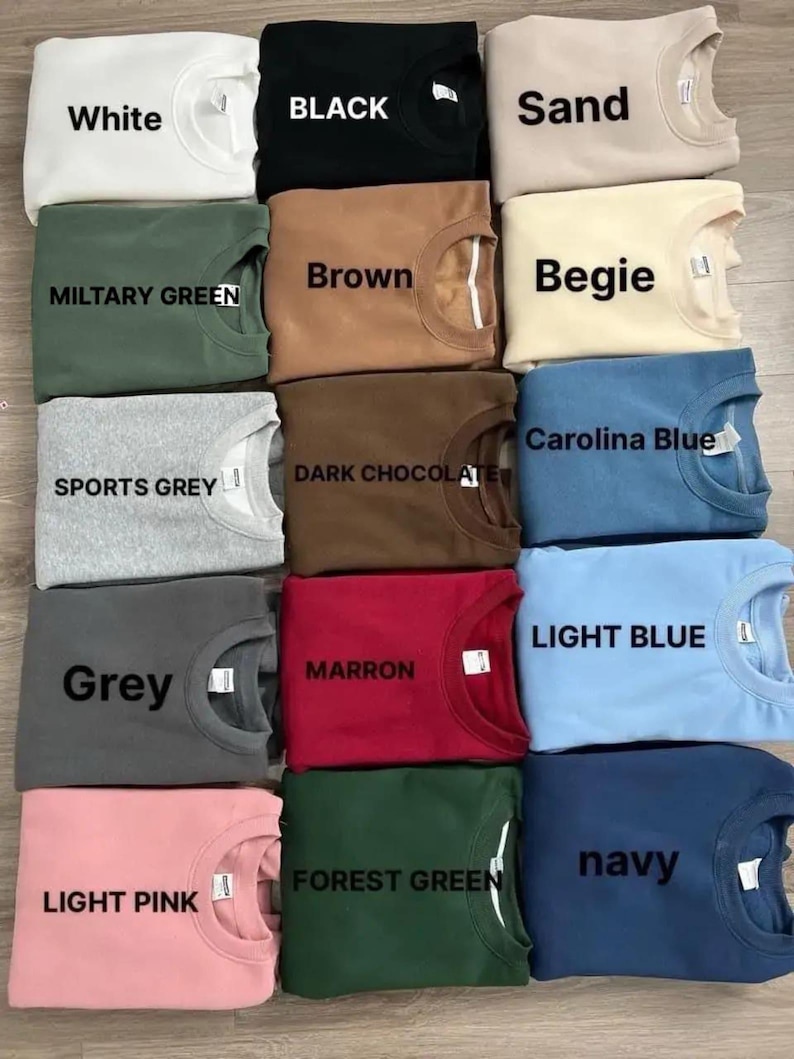 Puede incluir: Una colecci&oacute;n de sudaderas de cuello redondo dobladas en varios colores, incluyendo blanco, negro, arena, verde militar, marr&oacute;n, beige, gris deportivo, chocolate oscuro, azul Carolina, gris, granate, azul claro, rosa claro, verde bosque y marino. Cada camisa tiene una etiqueta.