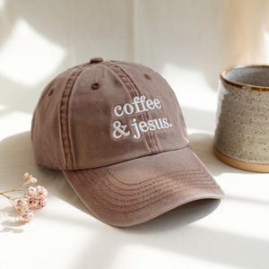 Op de afbeelding: Een bruine baseballcap met de geborduurde tekst "coffee & jesus." De cap heeft een gebogen klep en een klassiek zes-panelen ontwerp. De hoed is gemaakt van een zacht, versleten materiaal.